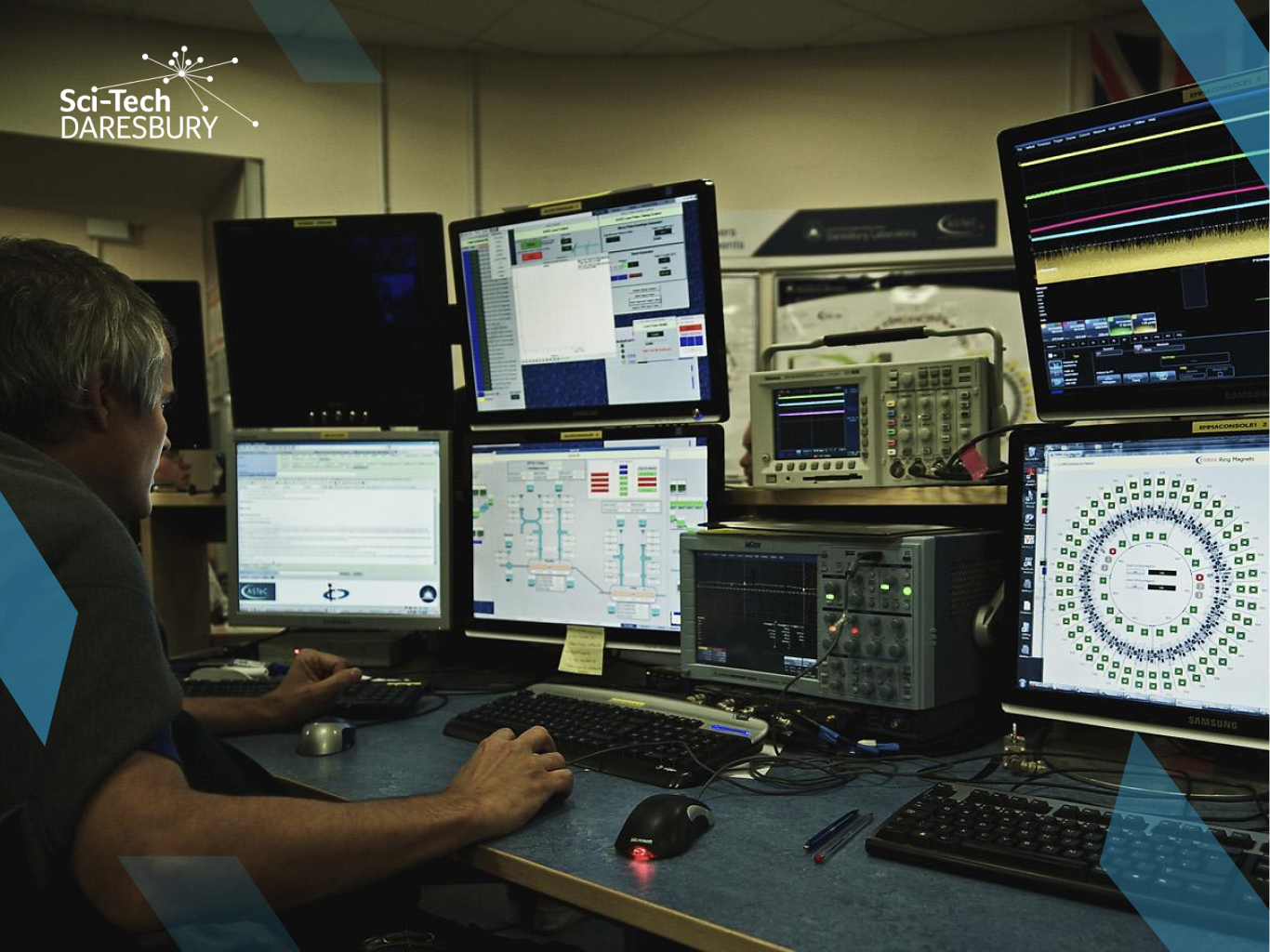 Photo of man working on scientific computers with all screens visible. Sci-Tech Daresbury logo in the top left corner.