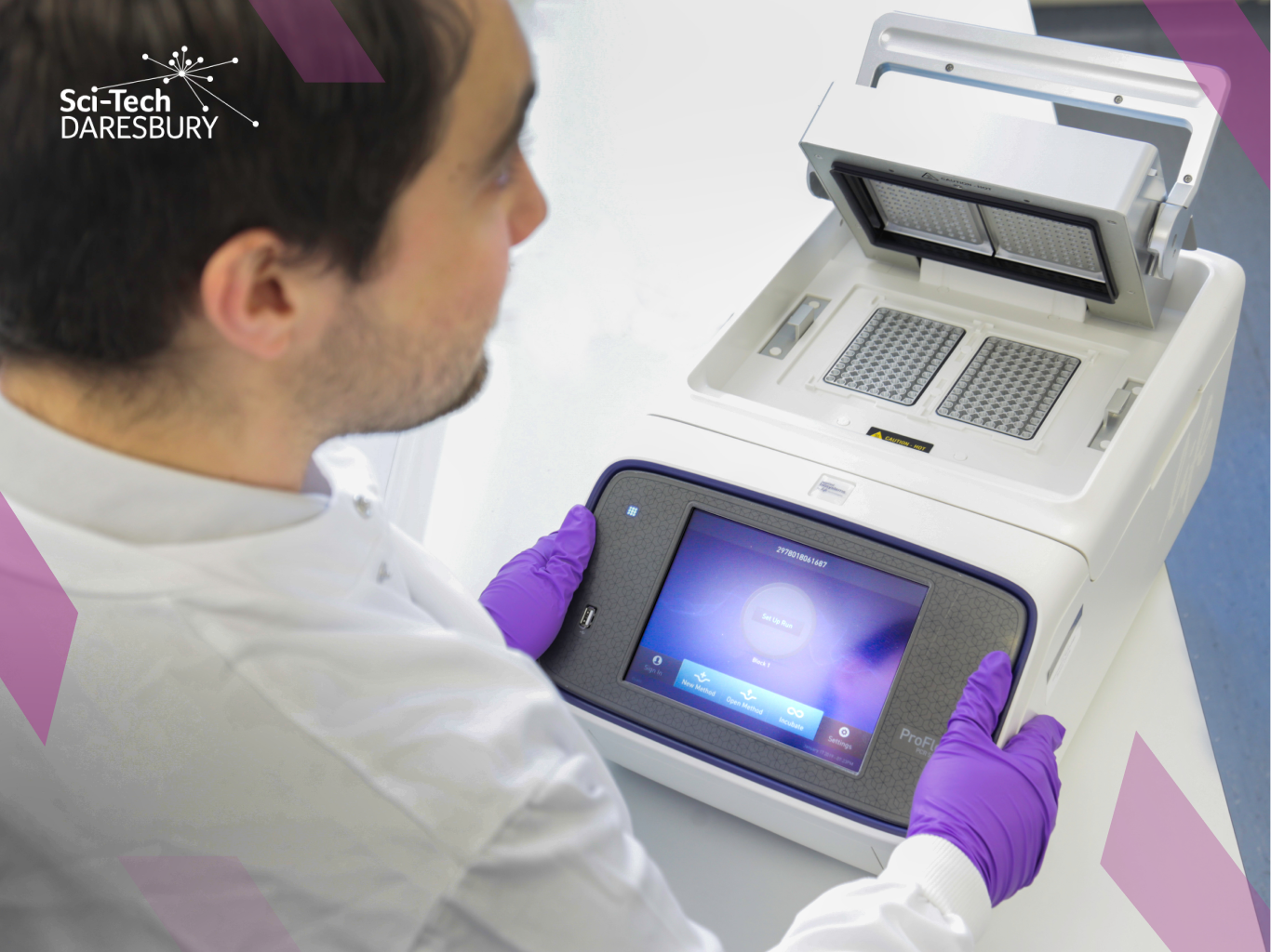 Photo taken from over the shoulder of a man dressed in a white lab coat, working on some scientific machinery looking at data.